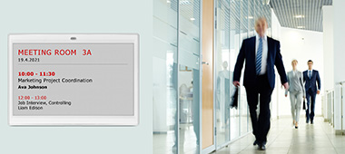 Room signage in the public sector using a LANCOM Wireless ePaper Display Room signage in the public sector by means of a LANCOM Wireless ePaper Display. A man wearing a suit and carrying a briefcase is walking along a corridor.